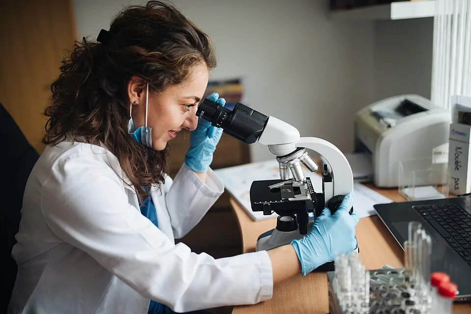 Context photograph: Lab technitian looking through the microscope while adjusting coarse knob; science context, not an identified product or supplier on this page.