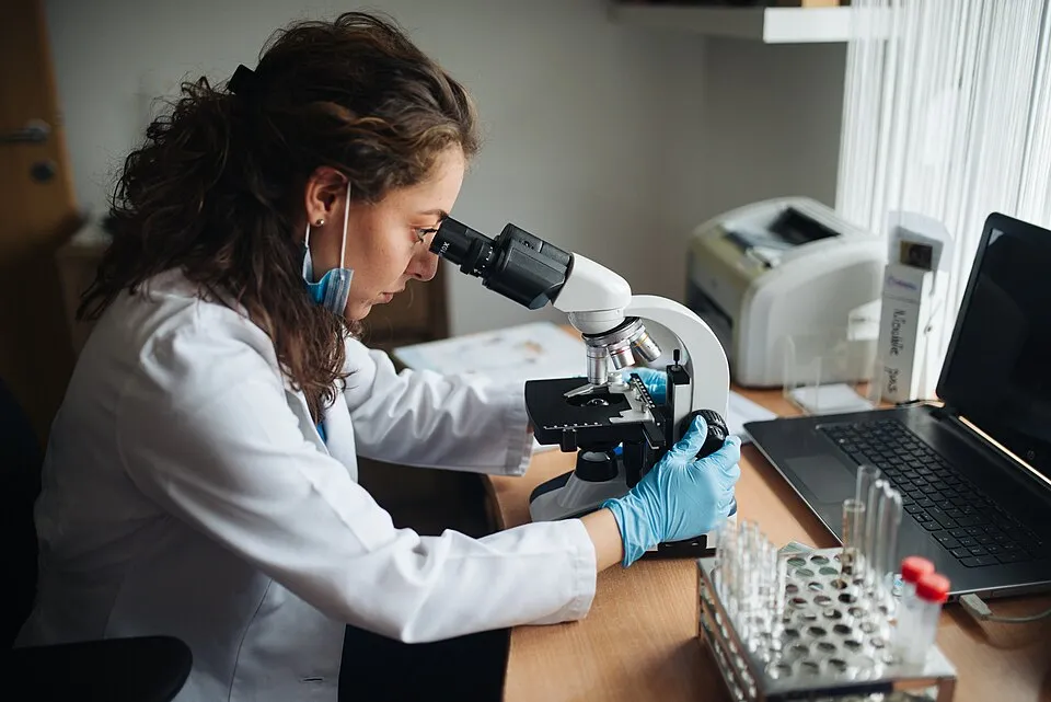 Context photograph: Lab technician looking through the microscope; science context, not an identified product or supplier on this page.