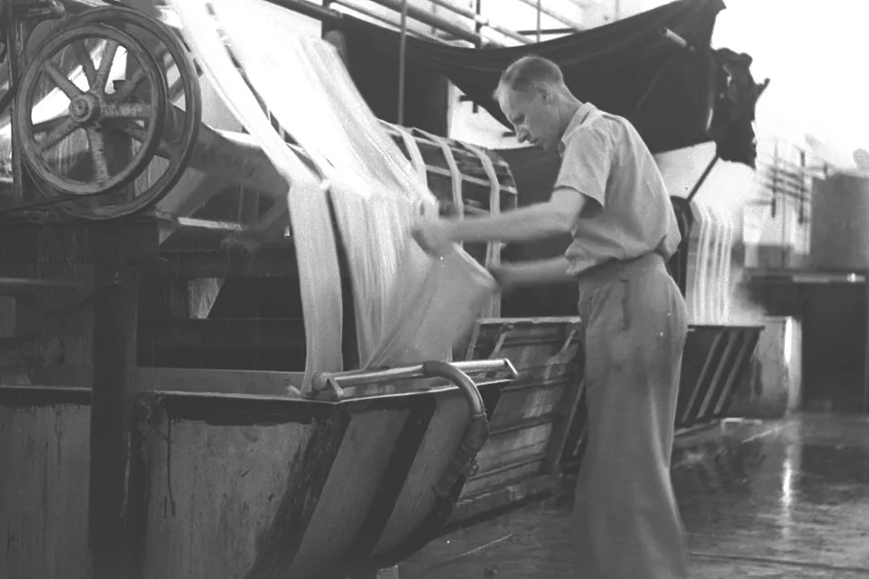 Context photograph: A WORKER IN FRONT OF A LOOM IN A TEXTILE FACTORY IN TEL AVIV. תעשייה. בצילום, פועל מפעיל מכונת אריגה במפעל טקסטיל בתל אביב.D19-039; textile context, not an identified product or supplier on this page.